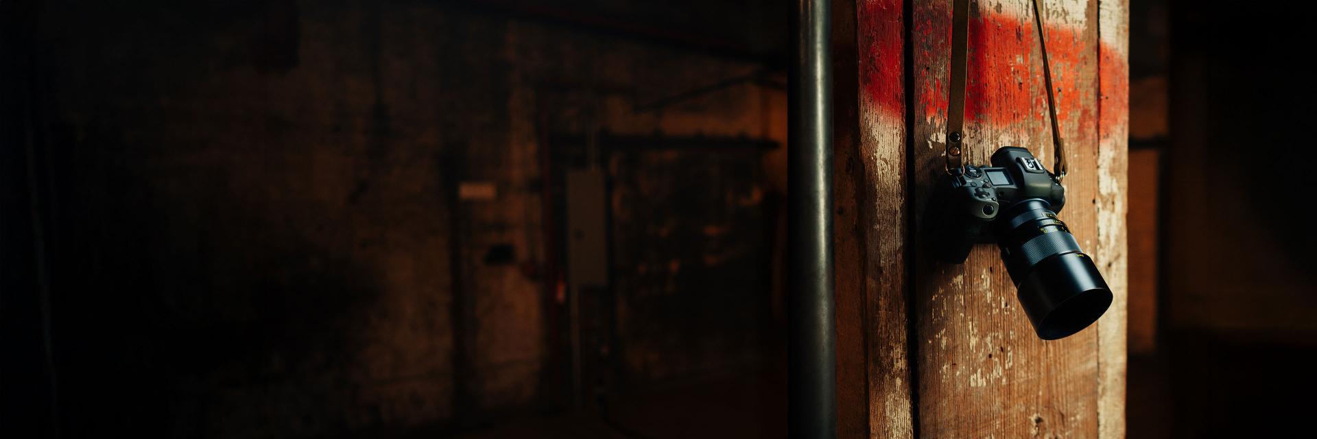 A ZEISS camera with a large lens is mounted on a wooden pillar in a dimly lit industrial setting.