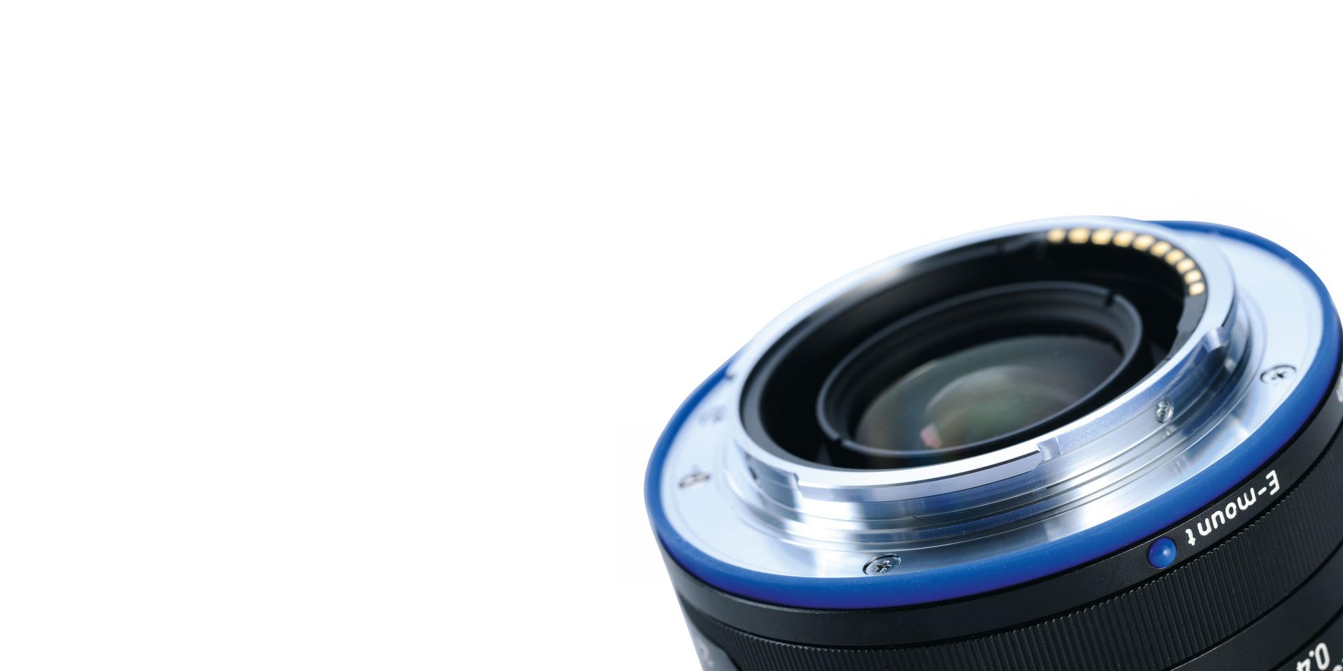 Close-up view of a ZEISS camera lens showing the metal mount, aperture ring, and focus markings.