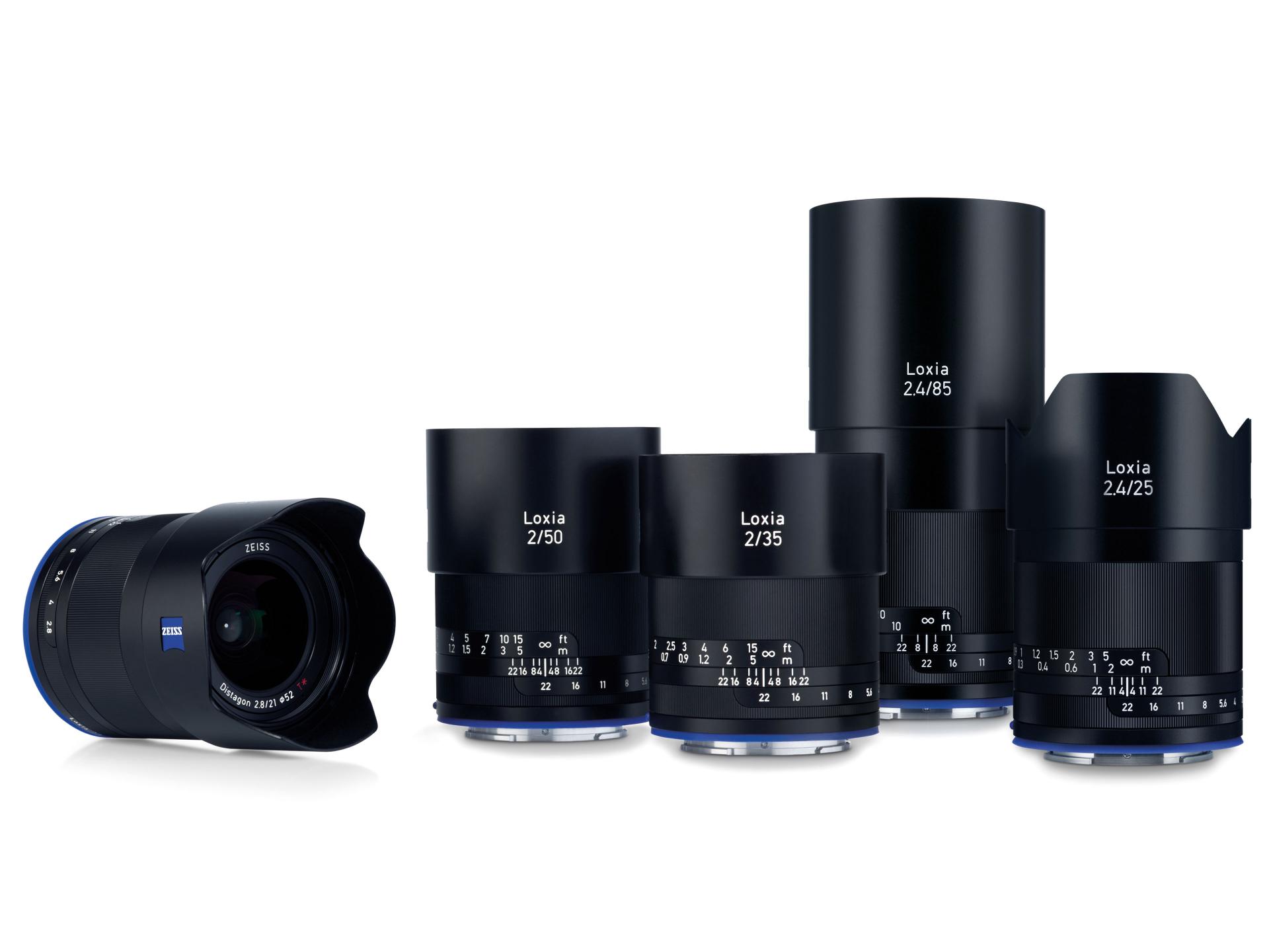 Five ZEISS Loxia camera lenses in various focal lengths are displayed standing upright, with one lens positioned lying down in front.
