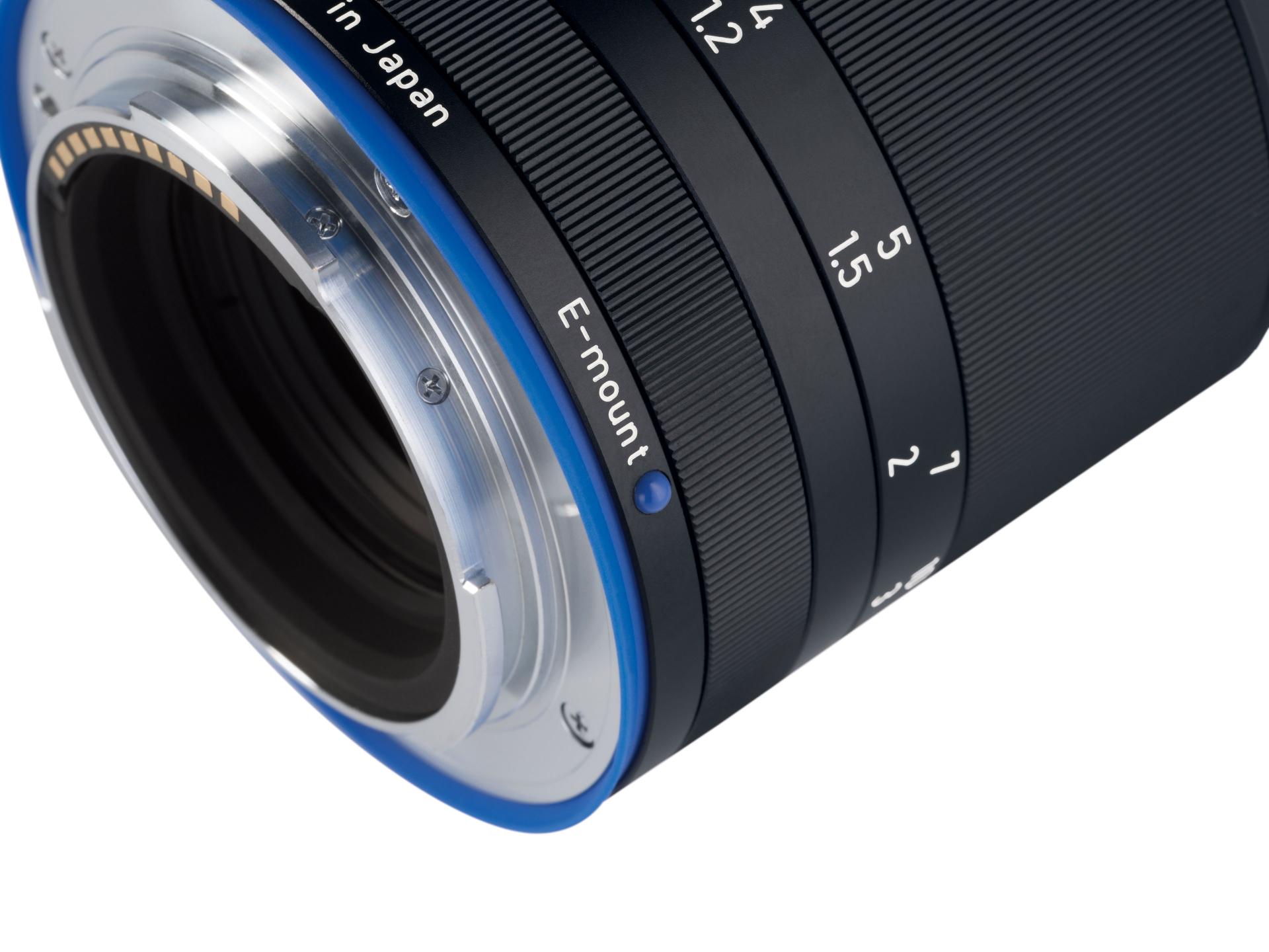 Close-up view of a ZEISS camera lens showing the E-mount, aperture markings, and precision metal construction.