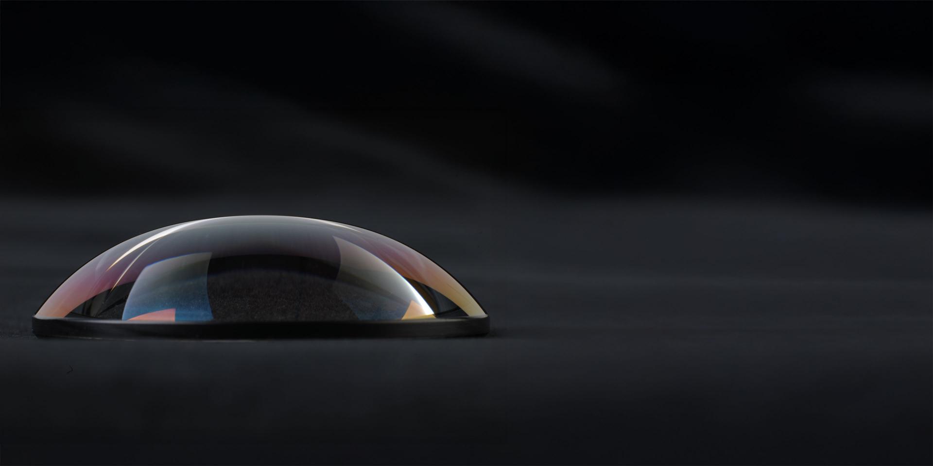 A close-up image of a high-precision ZEISS optical lens with a curved surface, set against a dark background.