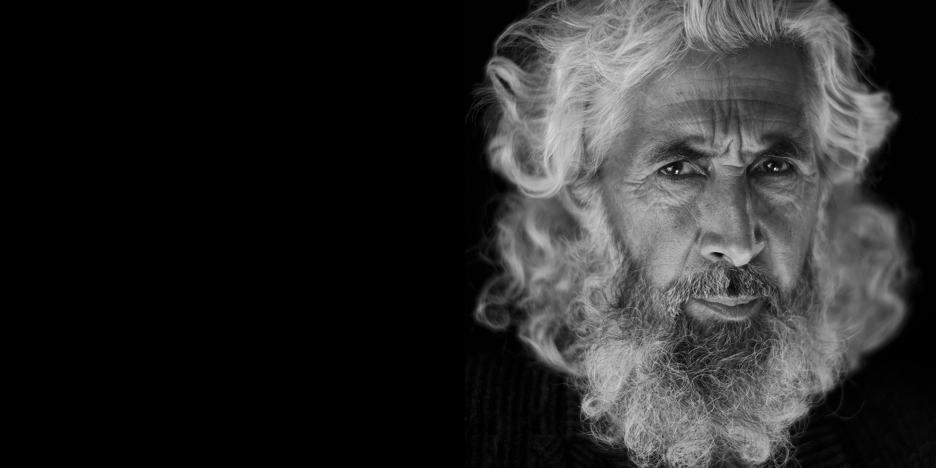 A dramatic black-and-white portrait reveals the deep textures and expressive character of an elderly man, highlighting the exceptional detail and contrast rendered by ZEISS lenses.