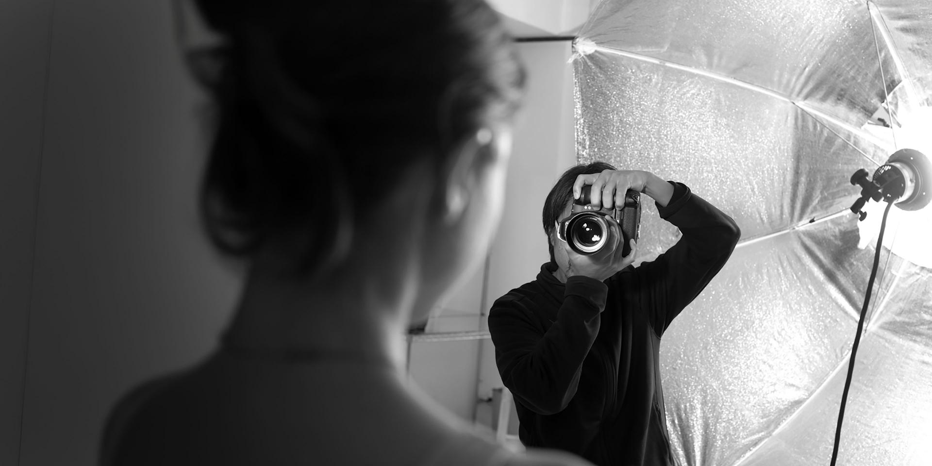 A photographer is capturing a portrait of a person using a camera equipped with a ZEISS lens.