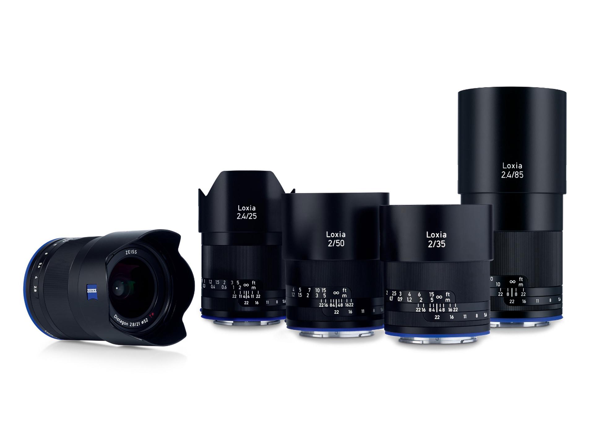 Five ZEISS Loxia camera lenses of varying focal lengths are displayed upright in a row, with one lens positioned horizontally in front.