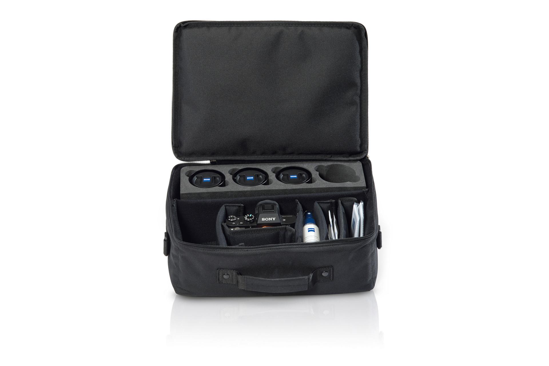 Open black camera bag containing multiple ZEISS camera lenses, a camera body, cleaning supplies, and accessories.