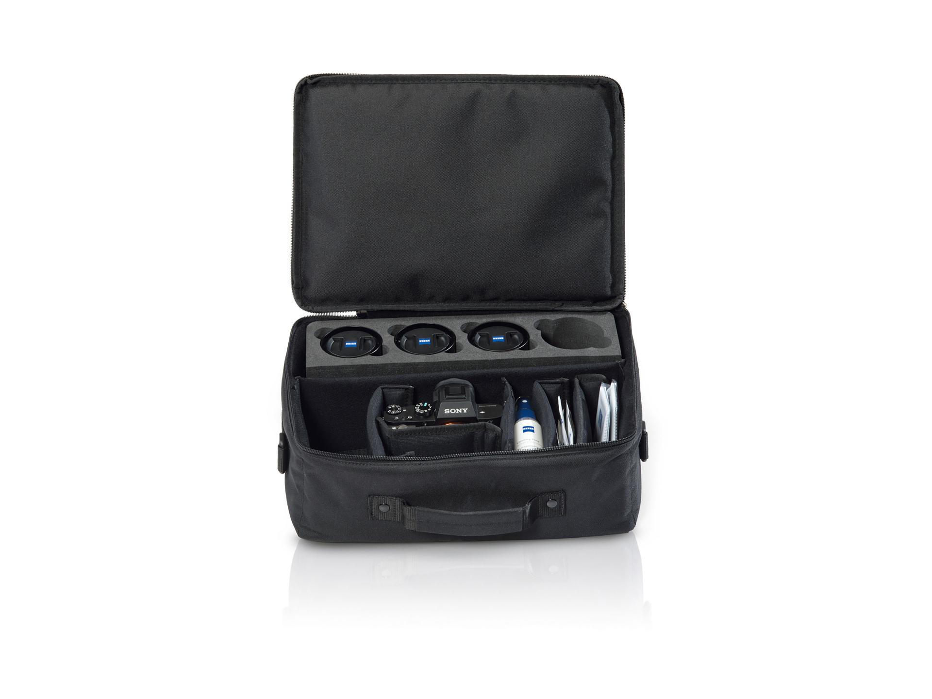 Open black camera bag containing multiple ZEISS camera lenses, a camera body, cleaning supplies, and accessories.