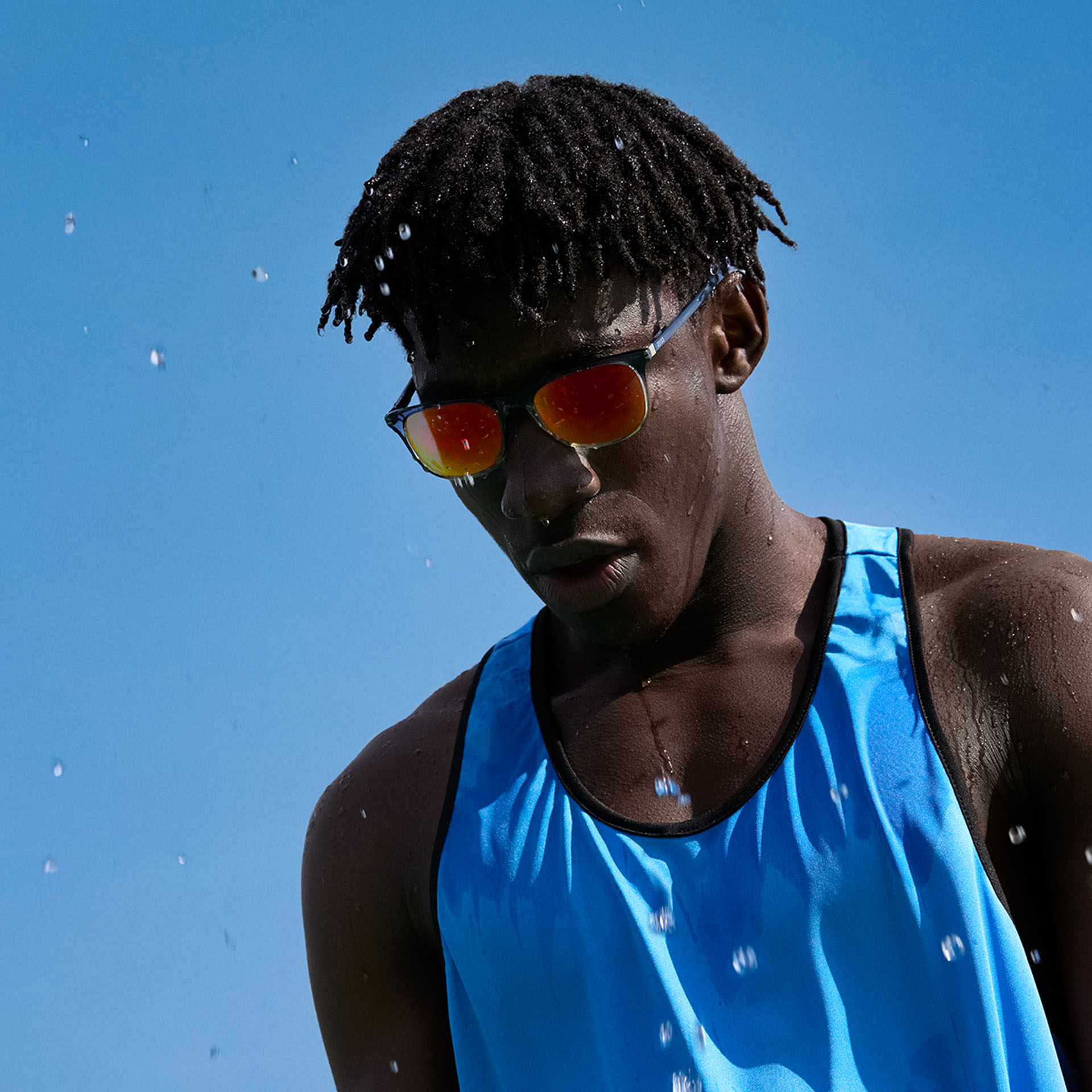 Een jonge man in sportkleding en ZEISS Performance zonnebrilglazen in een bruin-oranje tint tegen een blauwe lucht.