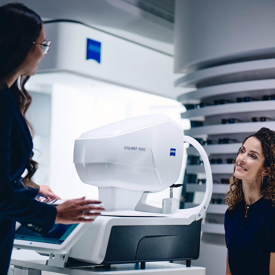 Een vrouw zit voor de ZEISS VISUREF 1000 en kijkt naar een vrouwelijke opticien.