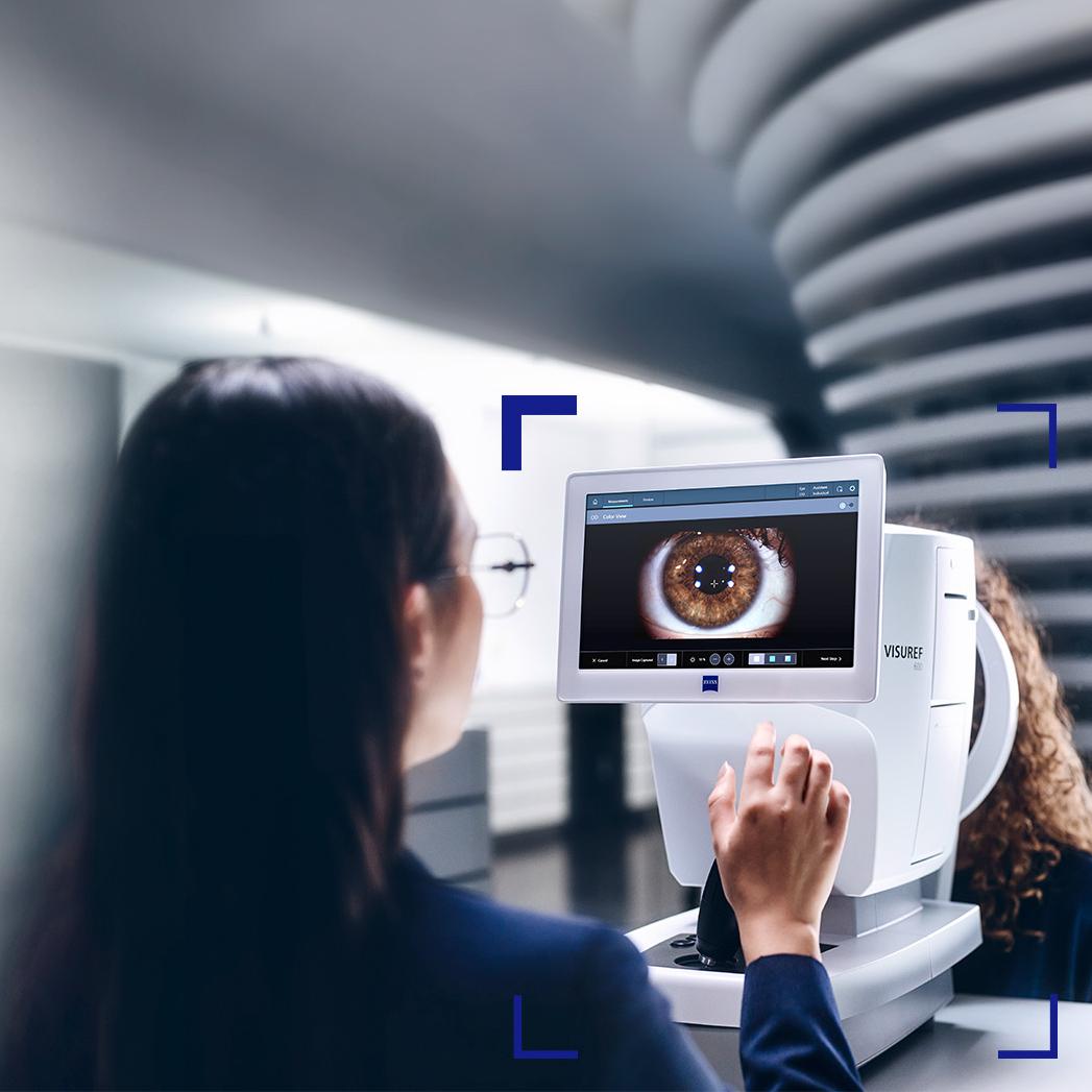 Een vrouwelijke opticien kijkt naar het scherm van de ZEISS VISUREF 600 waarop een beeld van een oog te zien is.