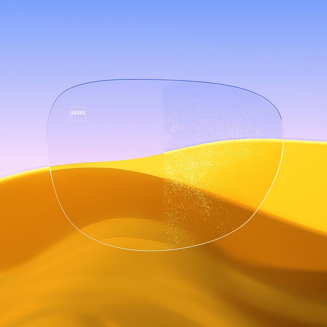 Een afbeelding met een gedeeld brillenglas waarvan de ene helft helder en schoon is dankzij ZEISS DuraVision Gold UV, terwijl de andere helft bedekt is met stof.