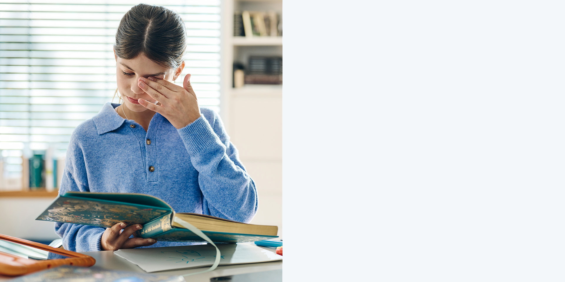 Meisje wrijft in haar ogen terwijl ze een boek leest.