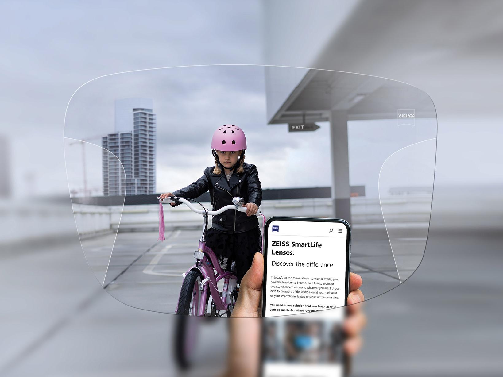 Persoon kijkt naar zijn telefoon door ZEISS progressieve SmartLife brillenglazen. Op de achtergrond zie je een meisje op haar fiets met een roze valhelm op. 