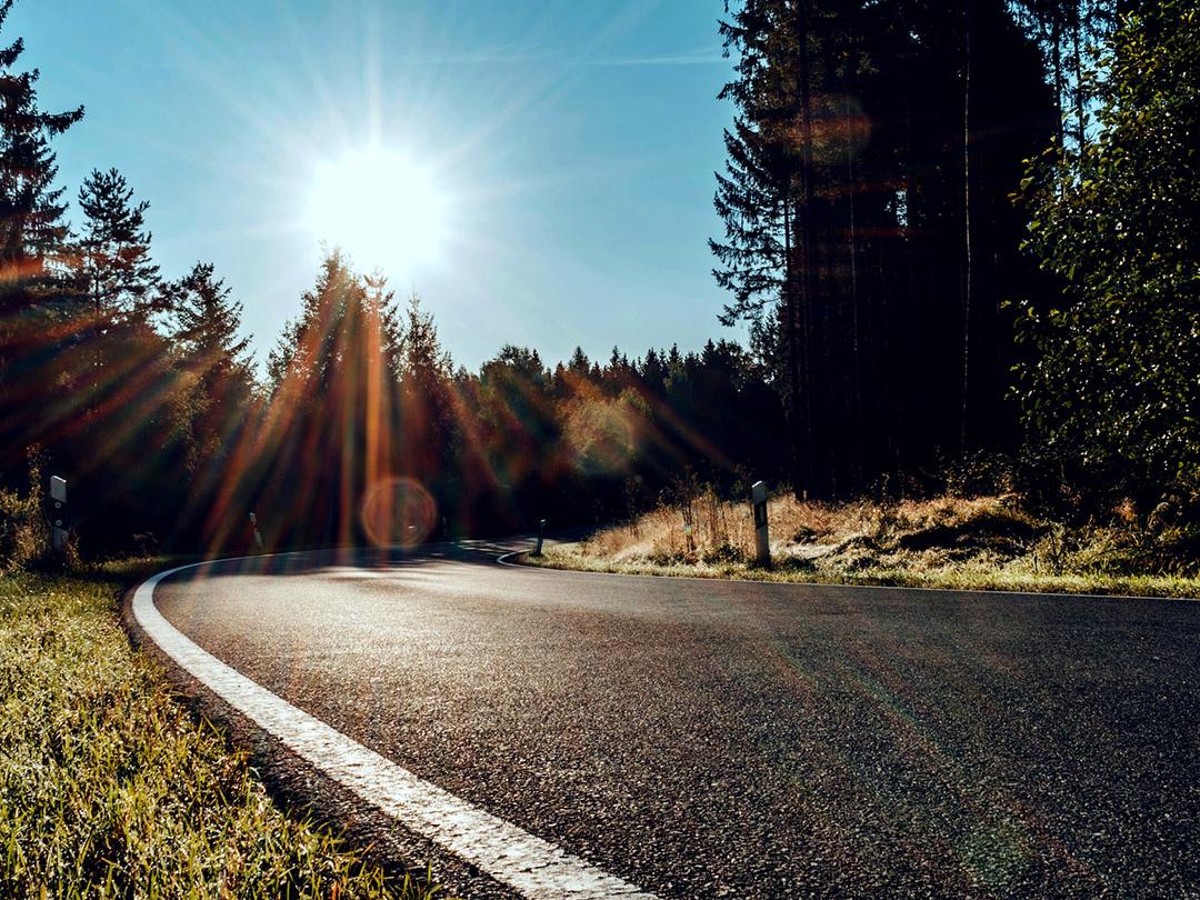Een sliderafbeelding waarbij de ene helft een weg in het bos toont met fel zonlicht, en de andere helft dezelfde weg toont met verminderde schittering en verhoogd contrast, wat het effect van gepolariseerde zonnebrilglazen benadrukt.
