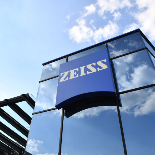 Een afbeelding van een modern glazen gebouw met een groot ZEISS logo erop. 