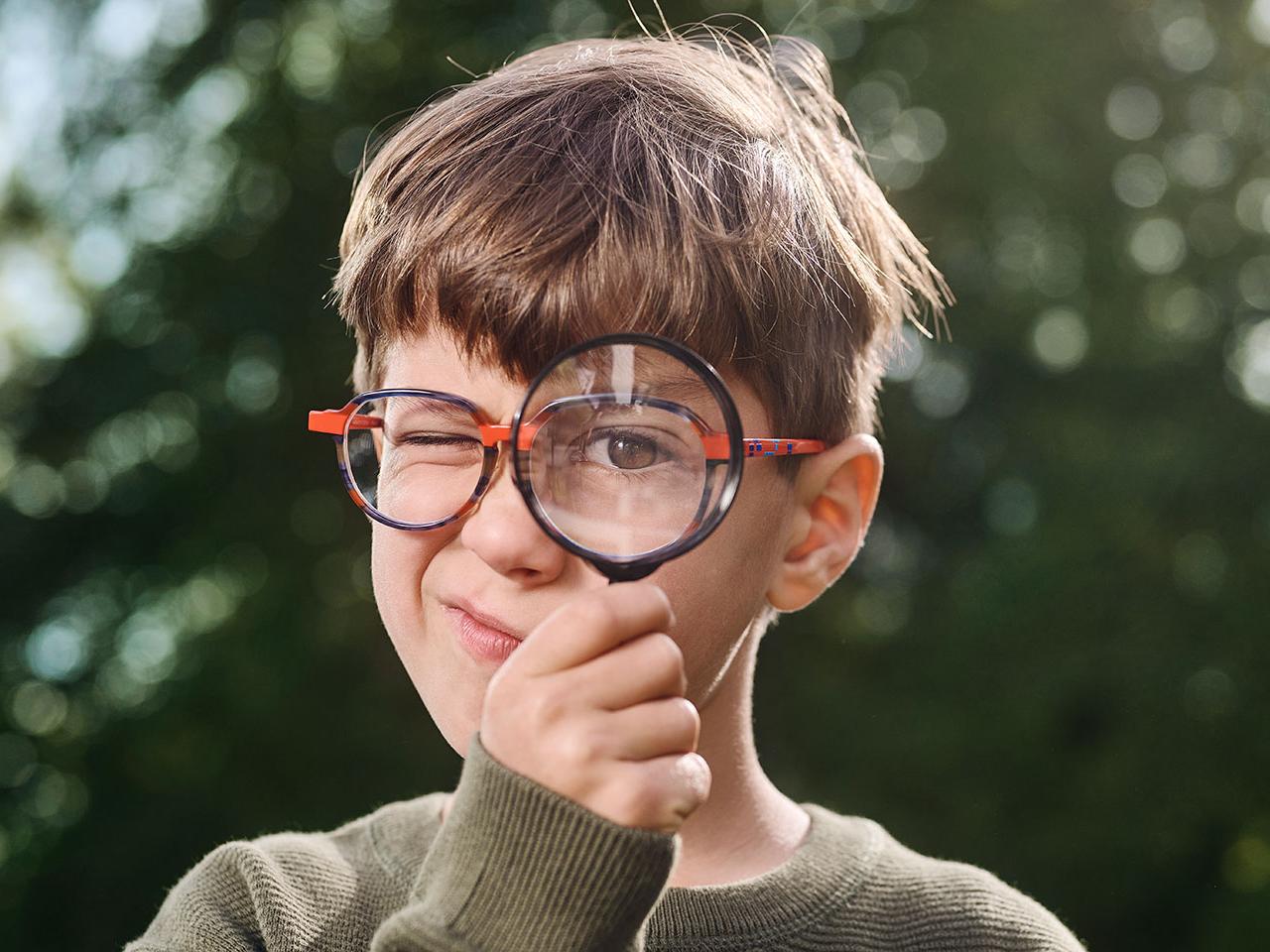 Jongen met bril die vergrootglas gebruikt 