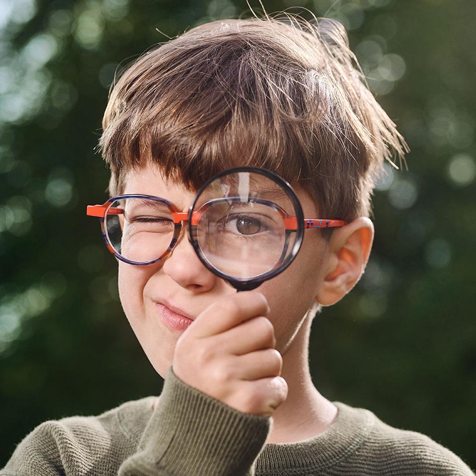 Jongen met bril die vergrootglas gebruikt 