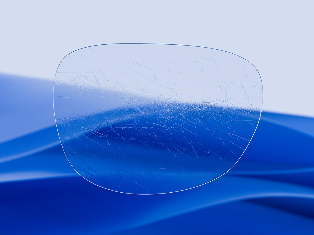 Gedeeld beeld met aan de ene kant een ZEISS brillenglas dat kenmerkend helder en schoon is, terwijl de andere helft een bekrast standaard brillenglas laat zien, wat het verschil in duurzaamheid illustreert. 