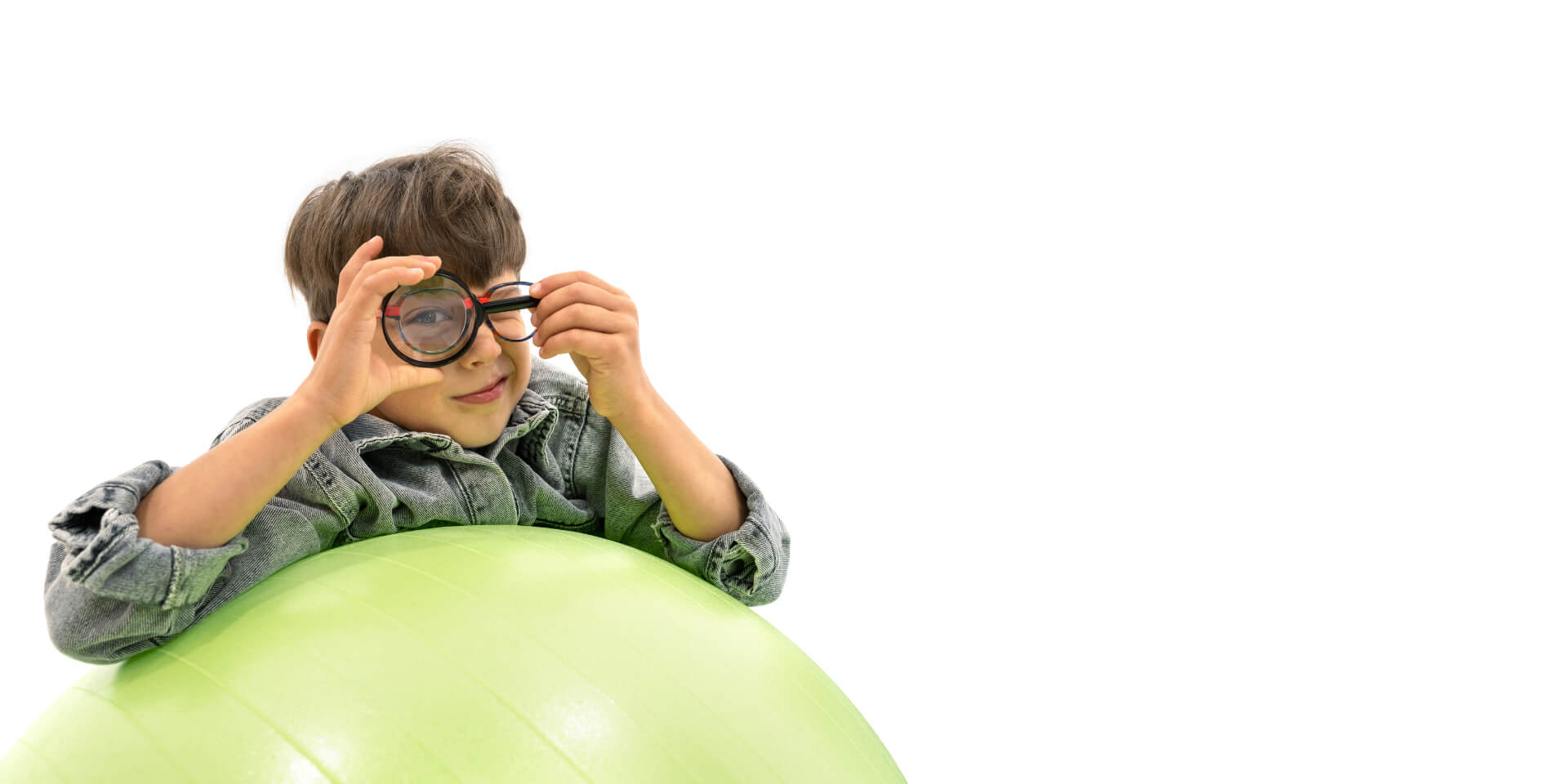 Een jongen met ZEISS brillenglazen voor myopie management leunt op een gymnastiekbal en houdt een vergrootglas voor één oog.