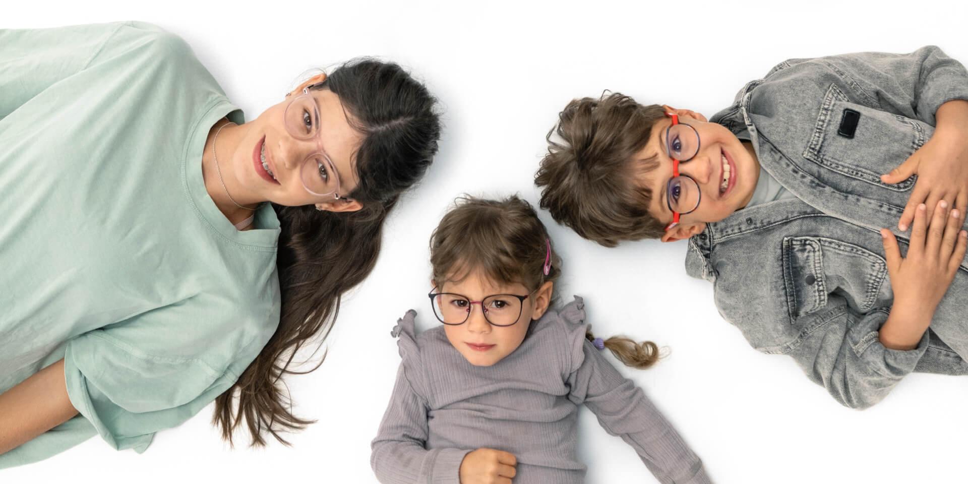 Een tiener en twee jongere kinderen liggen op de grond en dragen ZEISS myopie-brillenglazen.