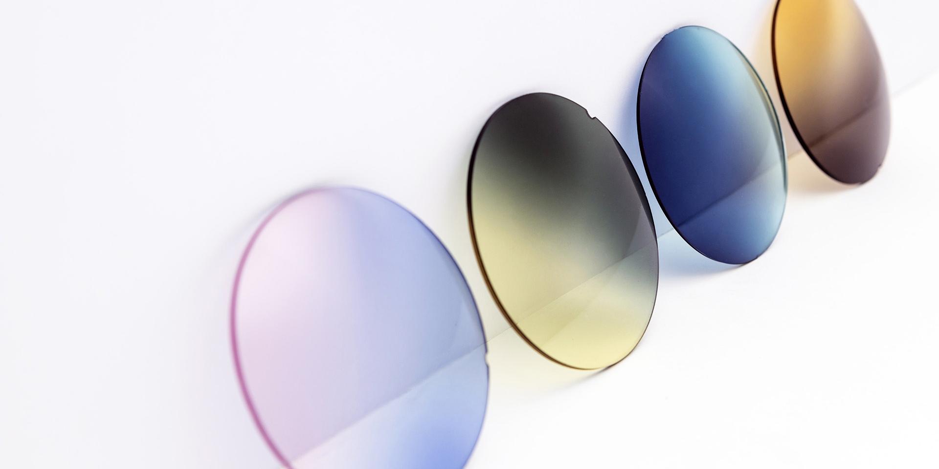 Verschillende gekleurde brillenglazen leunen tegen een wit oppervlak: roze-paars, geel-grijs, blauwe en bruine kleurverlopen.