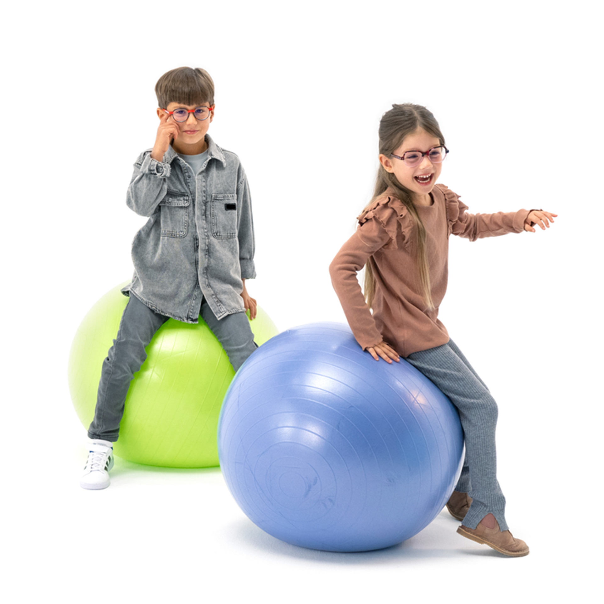 Een jongen en een meisje, die beiden een bril dragen, stuiteren speels op gymballen.