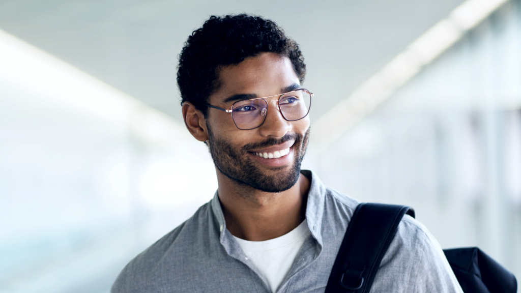 Een glimlachende jongeman met een rugzak over zijn schouder die een ZEISS Digital SmartLife bril draagt en opzij kijkt.